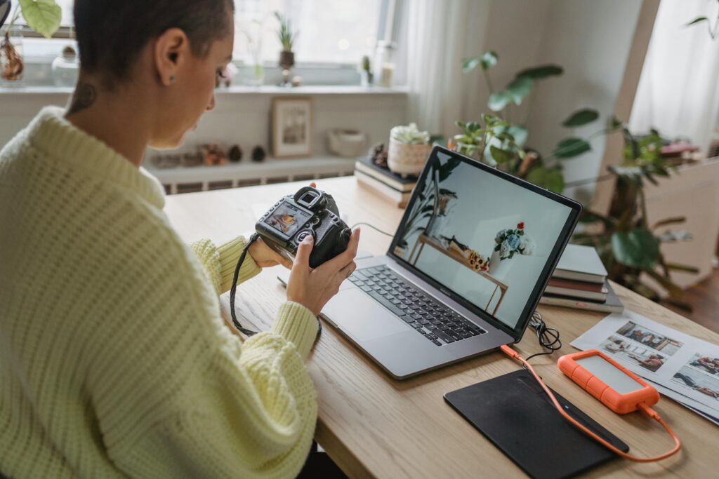 photographer looking at the viewfinder on her camera while sitting in front of her laptop.