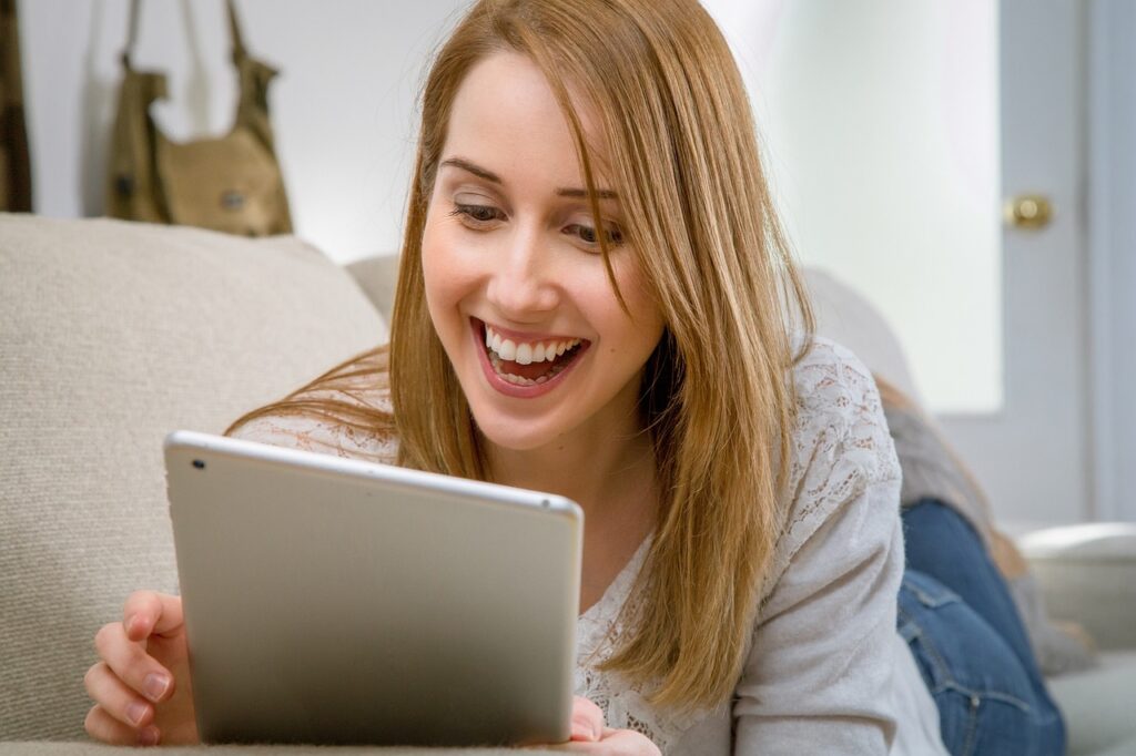 a woman smiling as she looks at her tablet