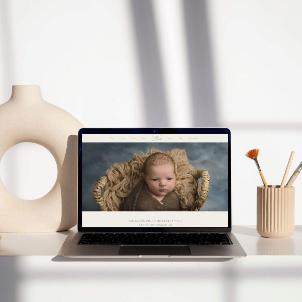 Picture of laptop on a table. Monitor has a picture of a newborn photography website on it.